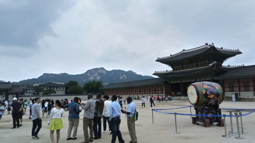 Gyeongbokgung Palace, Seoul, with lots of tourists in the foreground and the palace and mountains in the background.
